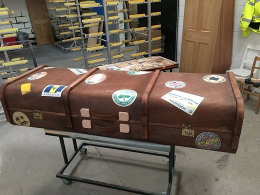 Rakev ve tvaru kufru, která je polepená zavazadlovými nálepkami z míst, které zesnulý navštívil.