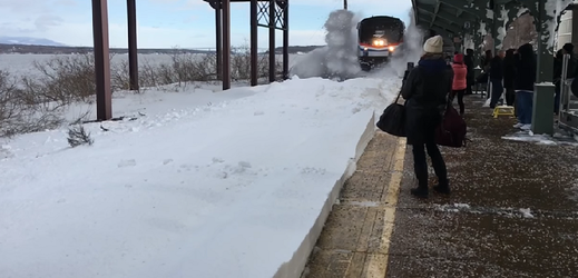 Vlak rozráží silnou vrstvu sněhu a míří k nástupišti. 