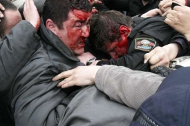 Zbitý policista se snaží ochránit v davu demonstrantů.