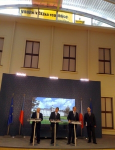 Premiér Fischer na tiskové konferenci, nahoře transparent Greenpeace.