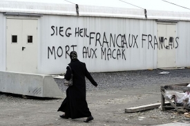 Žena míjí budovu u mešity postříkanou rasistickými nápisy.
