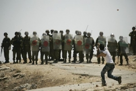 Palestinec hází kameny na izraelské vojáky.