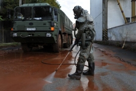Maďarský voják v protichemickém obleku čistí silnici pokrytou toxickým bahnem.