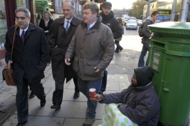 Zástupci Mezinárodního měnového fondu a Evropské banky procházejí kolem bezdomovce v ulicích Dublinu.