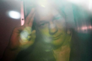 Assange za málo průhledným sklem při převozu k soudu v Londýně.