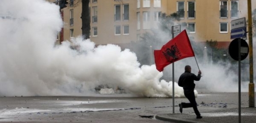 Demonstrant běží ulicí s albánskou vlajkou.