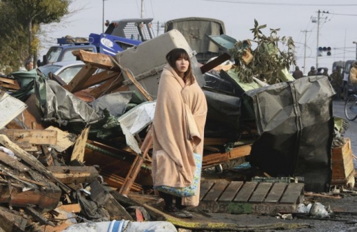 Žena zabalená v dece se dívá na trosky města Ishinomaki. 