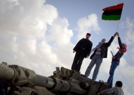Povstalci slaví na zničeném Kaddáfího tanku u Benghází.