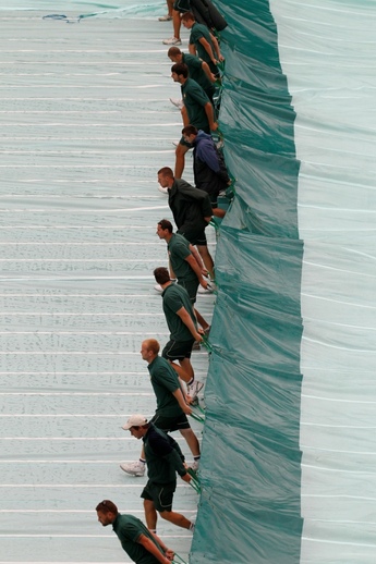 Dobrovolníci měli plné ruce práce s natahováním plachty nad wimbledonské trávníky. (Foto: ČTK)