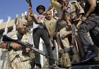 Rebelové pózují na soše Kaddáfího.