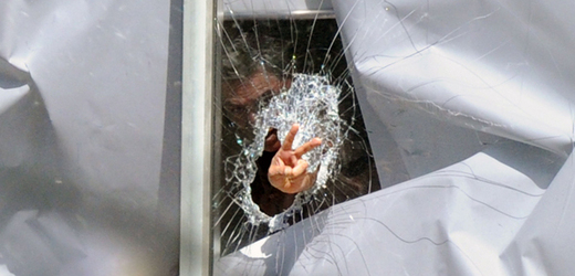 Muž gesty komunikuje skrze rozbité okno s policisty venku.