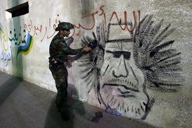 Bývalý libyjský rebel se trefuje botou o zeď, na které je nasprejovaný portrét Kaddáfího.