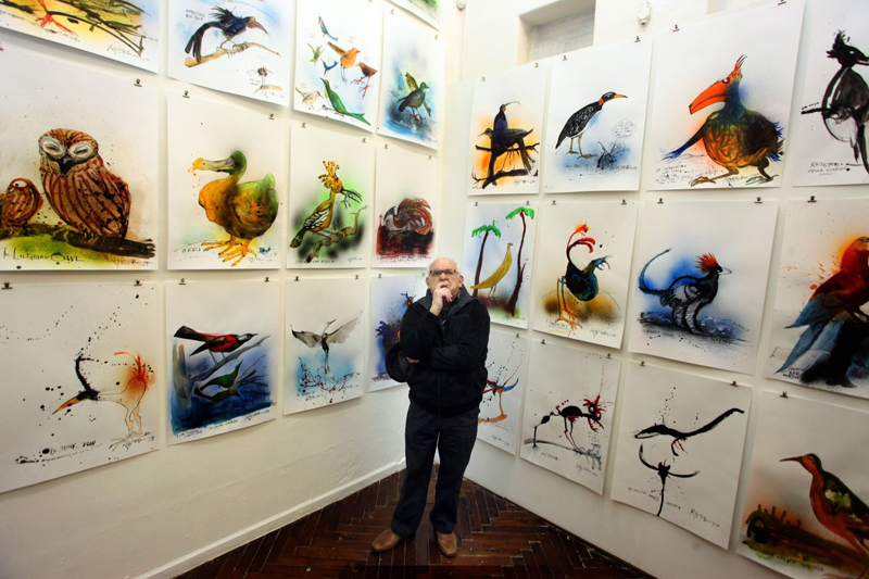 Zamyšlený umělec Ralph Steadman v obležení obrazů ptáků.