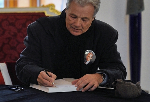 Muž s portrétem Václava Havla na hrudi se podepisuje do kondolenční listiny.