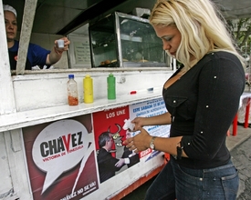Vnadná Venezuelanka u kiosku vyzdobeném plakátem na podporu prezidenta.