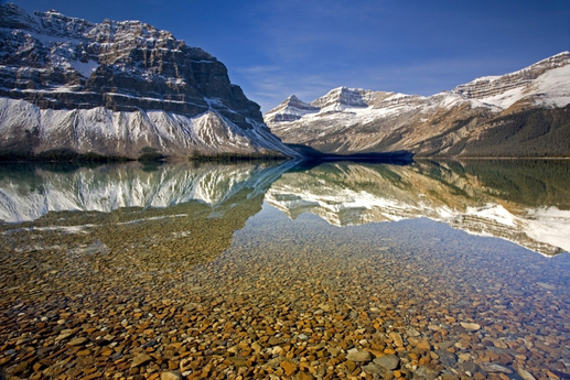 Dokonale čistá a nehybná hladina jezera Bow v kanadské Albertě odráží Crowfootské hory v pozadí. 