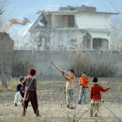 Abbottabádské děti hrají kriket, zatímco buldozer v pozadí demoluje dům, kde se Usama bin Ládin léta skrýval. 