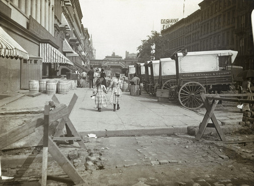 Dívky kráčejí po 42. ulici, vpravo stojí vozy obchodníků (1890).