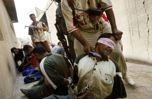 Sunnitský milicionář v Iráku drží nůž pod krkem podezřelého kajdistického ozbrojence.