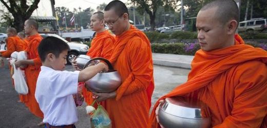 Thajský chlapec dává mnichům jídlo.