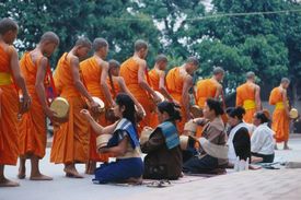 Lidé vkládají mnichům pokrmy do almužních misek.
