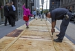 Pracovník údržby upevňuje překližky na chodníkové rošty budovami na Broadwayi v New Yorku. 