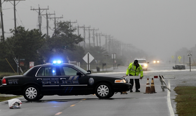 Policista staví zátaras na silnici v Nags Head ve státě Severní Karolína, kde hurikán způsobil zaplavení silnice. 