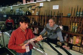 Muž si prohlíží kalašnikov v obchodu se zbraněmi.