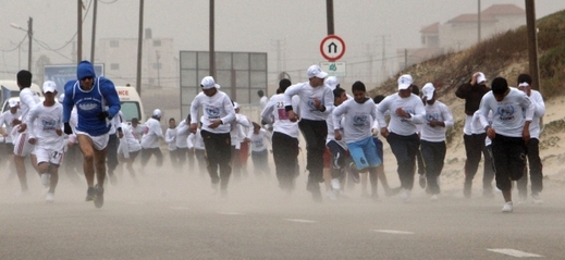 Maraton roku 2012. Běžci vzdorují větru na mořském pobřeží.