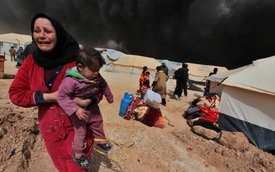 Žena utíká od hořícího stanu v uprchlickém táboře na území Sýrie.