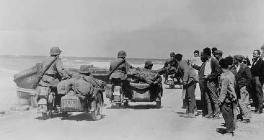 Řekové sledují s úsměvem německé vojáky z divize SS Leibstandarte Adolf Hitler, kteří jedou po pláži (snímek z roku 1941).
