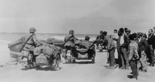 Řekové sledují s úsměvem německé vojáky z divize SS Leibstandarte Adolf Hitler, kteří jedou po pláži (snímek z roku 1941).