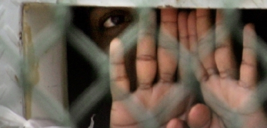 Fotografie vězně v zálivu Guantánamo, který se dívá ven tzv. fazolovou dírou. Používá se k předávání jídla. 