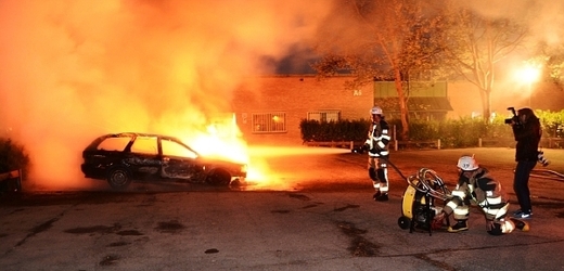 Hasiči likvidují požár hořícího auta ve švédském předměstí Husby.