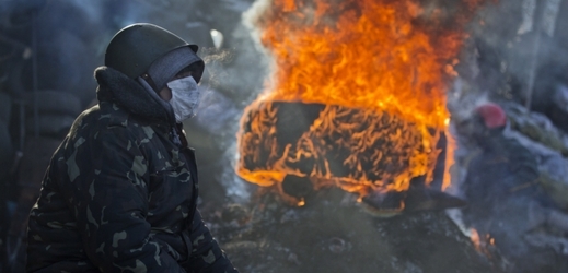 Demonstrant sedí vedle hořící barikády v centru Kyjeva.