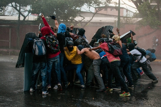 Opoziční demonstranti čelí proudům z vodního děla v Caracasu.