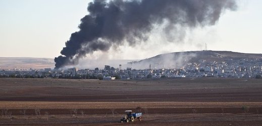 Traktor jede po poli, v pozadí hoří část města Kobani po útoku amerického letectva na pozice Islámského státu. 