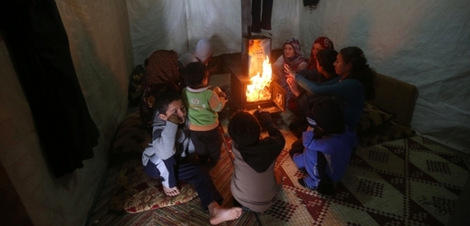 Syrští uprchlíci se ohřívají ve stanech v improvizovaném táboře.