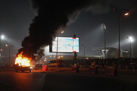 Hořící automobil před stadionem.