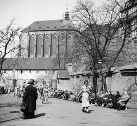 Lidé sedí na lavičkách před kostelem Panny Marie Sněžné v Praze (snímek z roku 1956).