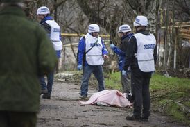 Pozorovatelé OBSE stojí u těla mrtvého ukrajinského vojáka poblíž obce Šyrokyne.