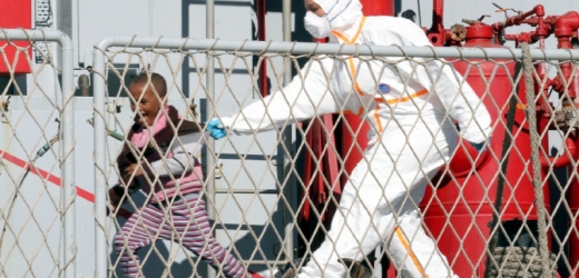 Sanitářka se snaží odchytit dítě, které do Itálie připlulo s ostatními uprchlíky.