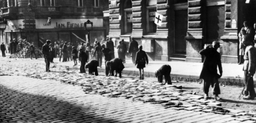 Německé děti, označené hákovým křížem, rozebírají barikádu a ukládají dlažební kostky zpět na vozovku. Žitná ulice v Praze, 1945.
