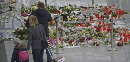 Cestující procházejí kolem svíček a květin na památku obětem pádu letadla. Letiště Düsseldorf.