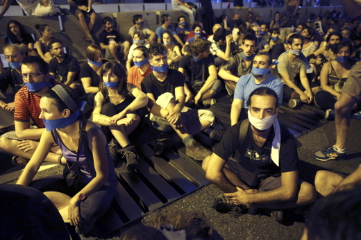 Lidé sedící před parlamentem ve Španělsku 30. června 2015 při protestech "People without Gag", které jsou namířeny proti novým zákonům, takzvaným "gag law". Schválila je poslanecká sněmovna už v prosinci roku 2014, ačkoli proti nim byla celá politická opozice. V platnost by měly vejít na konci července 2015.
