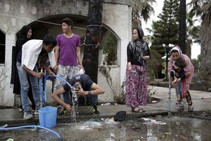 Migranti žijící v tábořištích se myjí pomocí zahradní hadice.