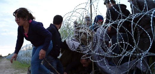 Migranti v Maďarsku prorážejí plotem z ostnatého drátu.
