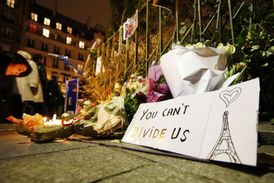 Věta "Nemůžete rozdělit nás" na pietní ceduli umístěné mezi rozsvícenými svíčkami a květinami v ulicí blízko divadla Bataclan v Paříži, Francie.