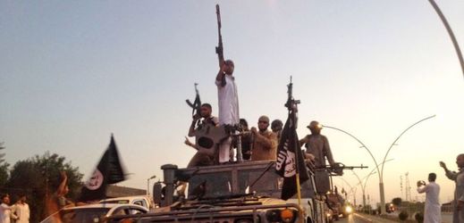 Bojovníci Islámského státu jedou na obrněném vozidle hlavní silnicí v severním městě Mosul v Iráku.