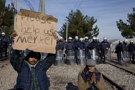 Uprchlíci označovaní za "ekonomické migranty" protestují a dovolávají se pomoci. Nápis na ceduli zní: Prosím, pomozte nám, Merkelová. Město Indomeni, Řecko.